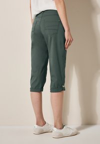 Green cropped pants made of lightweight fabric, with rolled cuffs and two back pockets. Paired with white sneakers on a neutral background.