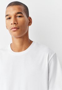 Tricou alb cu mâneci scurte și gât rotund, realizat din material neted. Prezintă un design minimalist și o croială lejeră.