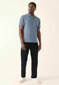Camisa polo de color azul claro hecha de algodón, con un cuello clásico y mangas cortas, combinada con pantalones negros y zapatillas blancas.