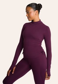 Paarse lange mouwen top met een neklijn en geplooide zijkanten, gemaakt van rekbare stof. Gepaard met bijpassende strakke leggings.