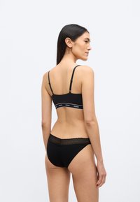 Braletă neagră cu bretele subțiri și bandă cu logo; chiloți negri asortați, cu dantelă și textură netedă, vizualizați din spate.