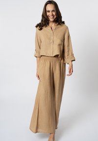 Completo in lino marrone chiaro composto da una camicia corta con bottoni e pantaloni a gamba larga con vita elasticizzata e maniche arrotolate.