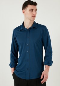 Sötétkék gombos ing sima anyagból, gallérral, hosszú ujjakkal és ívelt alsó résszel. A gombok feketék.
