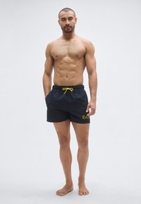 Fekete úszónadrág elasztikus derékrésszel és sárga húzózsinórral, a bal lábszáron sárga EAT logóval. Férfi úszóruházathoz tervezve.