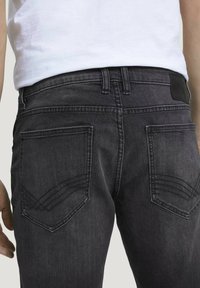 Musta farkut, joissa on slim fit -leikkaus, teksturoitu vyötärö, takataskut kaarevilla ompeleilla ja pieni nahkapatchi takana.