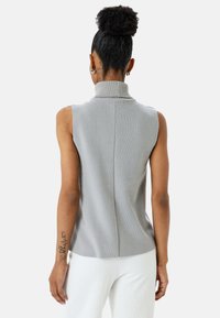 Lichtgrijze mouwloze turtleneck top met ribbeltextuur, voorzien van een hoge halslijn en een strakke achternaad, gecombineerd met witte textuurbroek.