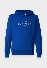 Felpa blu in morbido tessuto con tasca a marsupio, cappuccio con lacci e logo bianco "TOMMY HILFIGER EST.1985" sul davanti.