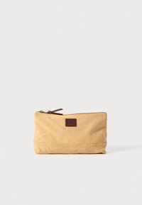 Pochette en toile beige avec fermeture éclair, accent en cuir marron et petite patch logo. Présente une forme rectangulaire et une texture durable.