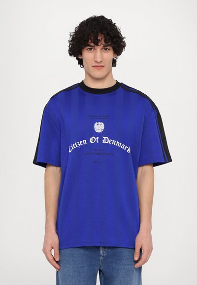 Blauwe oversized graphic t-shirt met zwarte schouderstrepen. Bevat tekst en een leeuwgrafiek op de voorkant, geribbelde zwarte halslijn.