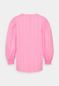 Blusa rosa com um padrão texturizado em riscas, apresentando mangas longas bufantes e punhos elásticos. Fecho com zipper nas costas, ao nível do pescoço.