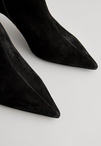 Black suede ankle boots with a pointed toe design, smooth texture, and visible stitching along the seams. No hardware or notable accents.