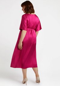 Fuchsia satin dress with short sleeves and a cinched waist, flowing to mid-calf length. Worn with nude heels. Smooth texture, solid color.