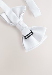 White bow tie made from textured fabric, featuring a black metal clasp and a flat, wide shape with pointed ends.