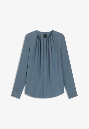 Blusa a maniche lunghe in morbido tessuto azzurro chiaro. Presenta pieghe sullo scollo e un orlo arrotondato. Polsini abbottonati e un design semplice ed elegante.