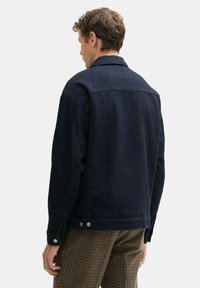 Dunkelblaue Jeansjacke mit klassischem Kragen, geknöpften Manschetten und detailliertem Rückeneinsatz, kombiniert mit karierten Hosen.