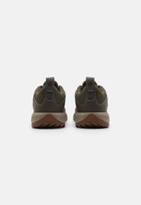Ciemnozielone buty sportowe z teksturowanej tkaniny, brązowe gumowe podeszwy i uchwyty z tyłu, charakteryzujące się smukłym designem.