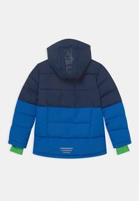 Veste rembourrée avec un haut bleu marine et un bas bleu. Comprend une capuche, des poignets de manches verts et des accents réfléchissants au dos.