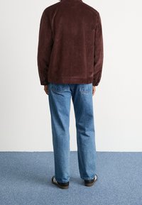 Mörk vinröd kordjacka med avslappnad passform, kombinerad med ljusblå denimjeans och svarta skor med vita ränder.