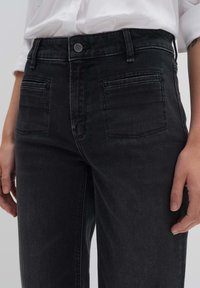 Musta denim korkeavyötäröinen farkut etutaskuilla, hienovaraisella tekstuurilla ja metallinappikiinnityksellä; suora lahje ja minimaalinen ompelu. 