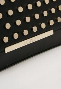 Surface en cuir noir avec des clous ronds en or espacés uniformément et une plaque rectangulaire en or gravée MLX&Co.