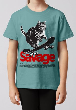 Kind trägt türkisfarbenes Shirt mit Grafik einer Katze, die auf einem Skateboard springt, über dem Wort "Savage" in rotem Text.
