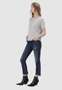 T-shirt gris à manches courtes associé à un jean skinny bleu foncé, avec un ourlet effiloché, et des bottines noires à bout pointu et à talon large.