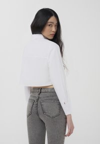 Camicia bianca cropped con colletto, maniche lunghe e bottone ai polsini, abbinata a jeans in denim grigio a vita alta con tasche posteriori.