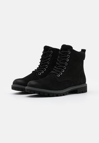 Une paire de bottines en suède noir à lacets avec des cols rembourrés et des semelles en caoutchouc robustes sur un fond blanc.