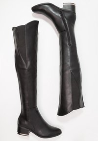 Bottes noires à hauteur de genou en cuir avec une finition lisse, dotées d'une fermeture éclair sur le côté et d'un talon bloc bas pour un meilleur soutien.