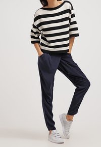 Pasiakowy czarno-biały oversize'owy sweter, zestawiony z granatowymi spodniami typu tapered i jasnoszarymi sneakersami. Luźny krój, fakturowany materiał.