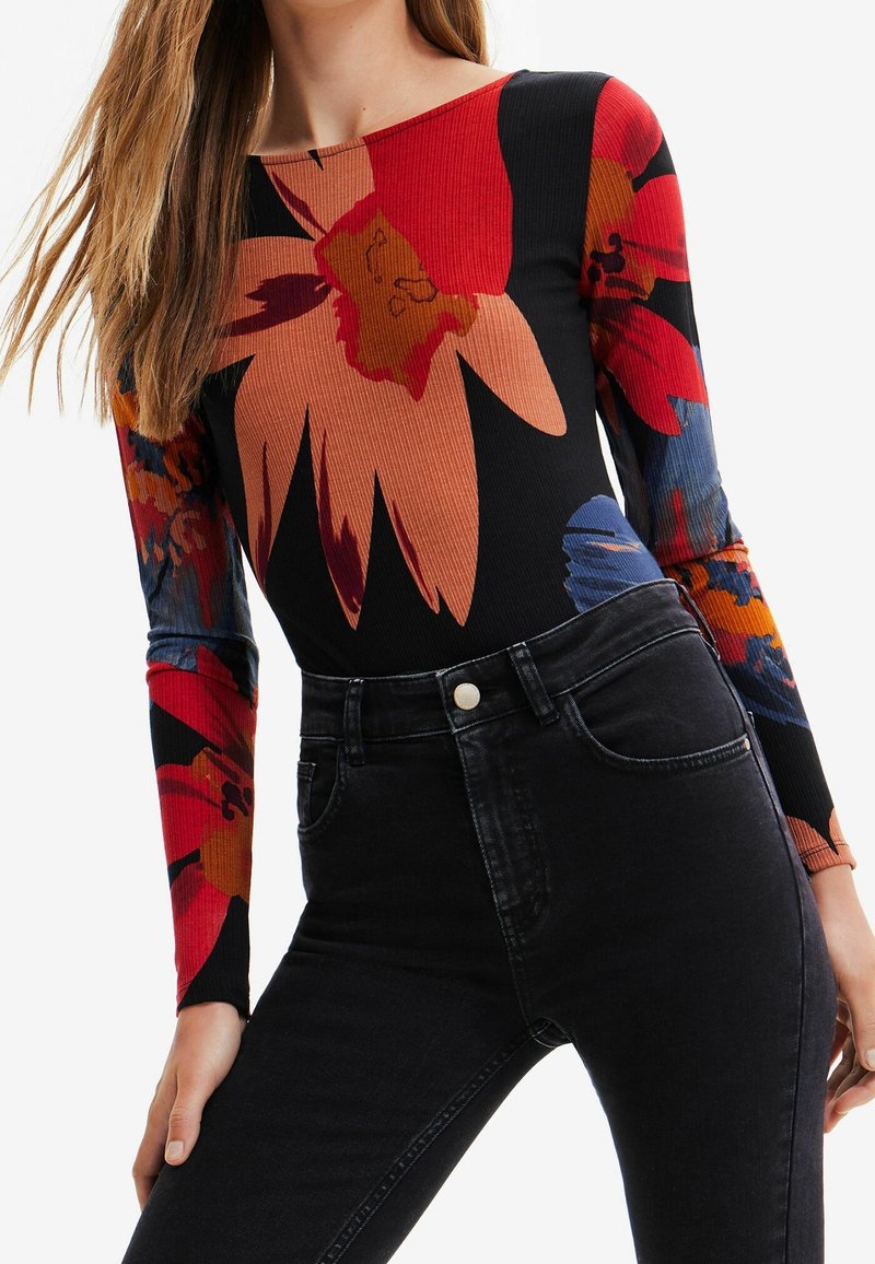 Long-sleeve bodysuit in black with large red and blue floral patterns; ribbed texture. Paired with high-waisted black jeans.