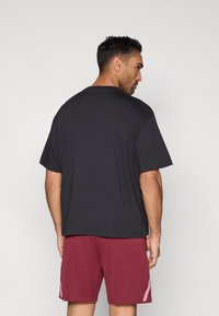 Must lühikeste varrukatega T-särk, mille lõige on lõdvestunud, näidatud tagantpoolt, koos burgundi spordipükstega, millel on küljes detailid.