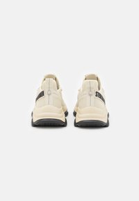 Sneaker color crema con tomaia in rete, suola in gomma nera e marchio nero a contrasto sulla linguetta del tallone. Design minimalista con linguette per il sollevamento.