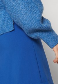 Blauer gestrickter Pullover mit gerippter Textur, kombiniert mit einem einfarbigen blauen Rock aus glattem Stoff. Das Outfit zeigt kontrastierende Blautöne.
