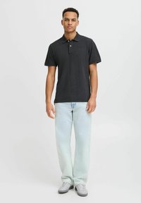 Svart poloshirt med en treknappslukking og korte ermer, kombinert med lyseblå jeans. Skjorten har en subtil logo-detalj.