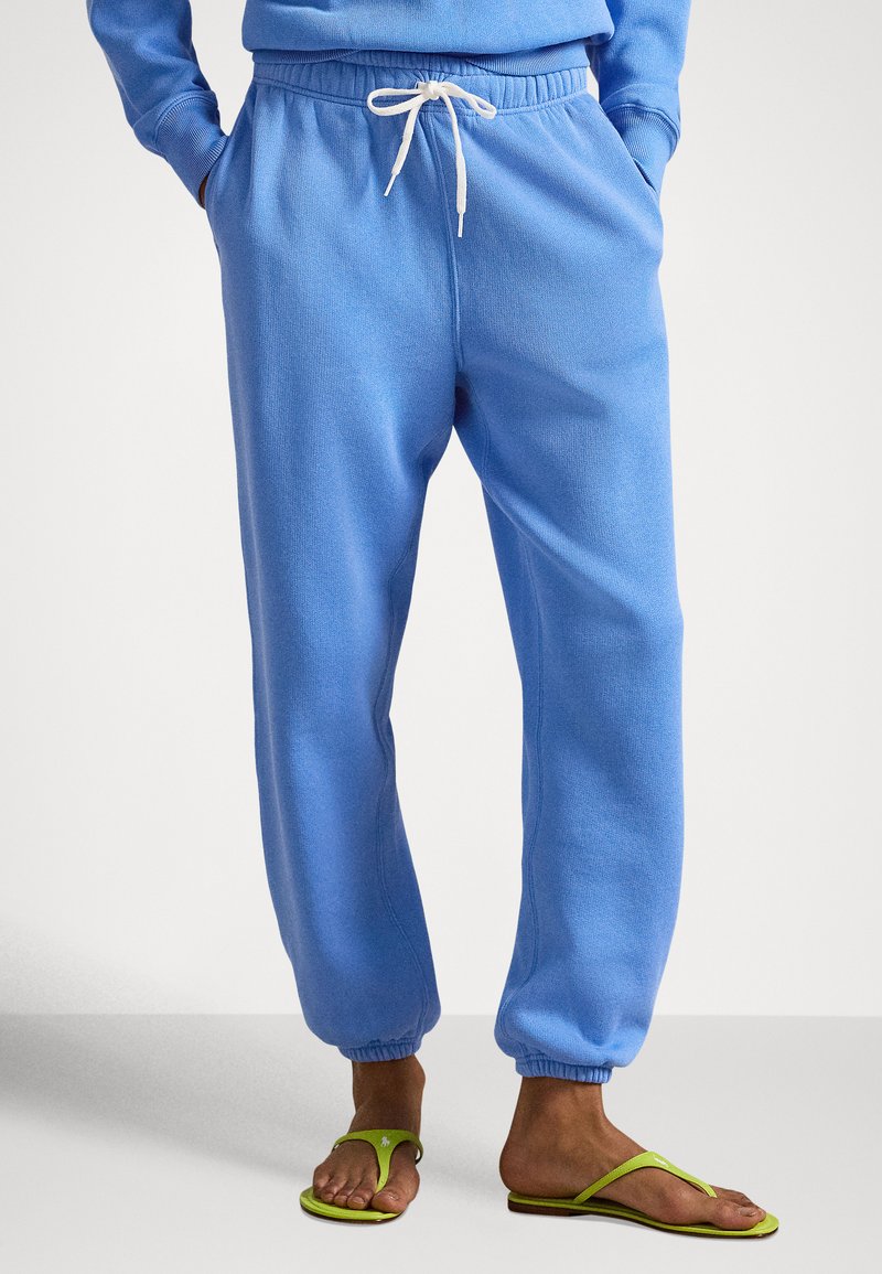 Lys blå joggebukser laget av mykt stoff, med elastisk midjebånd med snor og innsnevrede mansjetter; kombinert med grønne flip-flops.