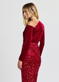 Haut en velours rouge à manches longues associé à une jupe à sequins ornée de différentes tailles de sequins rouges, créant un effet texturé et scintillant.