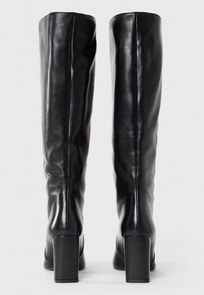 Black leather knee-high boots with a smooth texture, block heels, and a fitted design. The back shows a minimalistic, elegant silhouette.