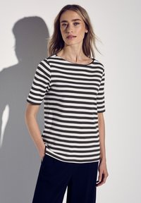 Camiseta de manga corta a rayas blancas y negras con cuello barco, con un corte relajado y tela suave, combinada con pantalones oscuros.