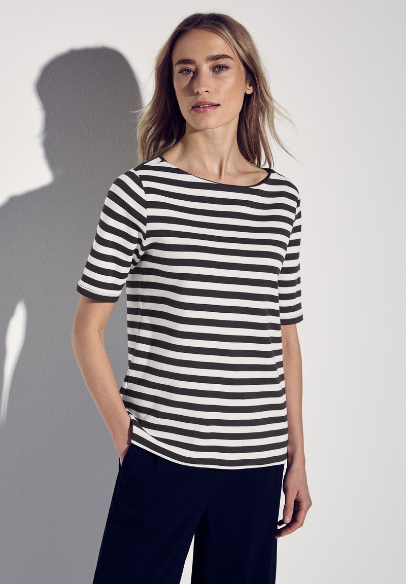 Camiseta de manga corta a rayas blancas y negras con cuello barco, con un corte relajado y tela suave, combinada con pantalones oscuros.