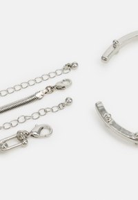 Silver-tone metal accessories including chains, clips, and a curved bracelet, featuring smooth surfaces and small spherical accents.