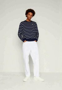 Pulover cu dungi bleumarin și alb, cu un design scurt, cu manșete și tiv râuri, asortat cu pantaloni albi largi și pantofi ușori.