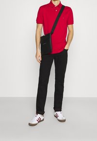 Punainen polo-paita, mustat housut ja valkoiset lenkkarit punaisilla yksityiskohdilla. Musta olkalaukku etutaskulla. Yksinkertainen muotoilu, rento tyyli.