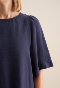 Top in lino blu navy con maniche corte a palloncino e scollatura rotonda, caratterizzato da una texture morbida e una vestibilità comoda.