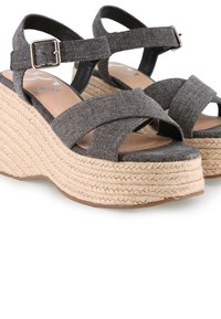 Sandalias de cuña de mezclilla gris con diseño de tiras cruzadas y hebilla ajustable en el tobillo. Presentan una plataforma de yute texturizado y una suela lisa.