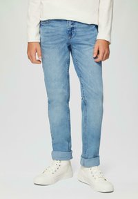 Gaiši zili džinsi ar šauru fitu, ar vidēju jostasvietu un sarullētām malām. Apvienoti ar baltām kanvas kedām.