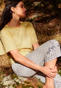 Geel T-shirt met korte mouwen, gemaakt van zachte stof, gecombineerd met gemêleerde capri-legging met bloem- en geometrische patronen in blauw en wit.