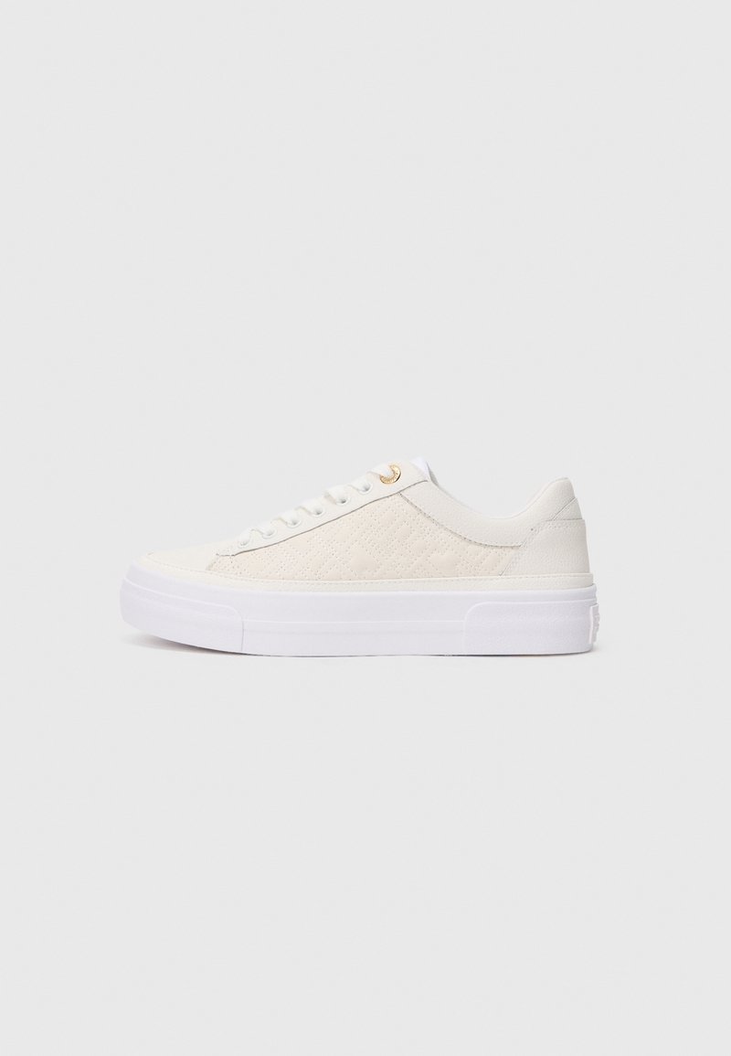 White sneaker with a textured fabric upper, smooth leather accents, flat white laces, and a thick white rubber sole. Gold-tone eyelet detail.