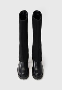 Black knee-high boots with a ribbed fabric upper and a smooth leather lower section. Chunky sole and rounded toe design.