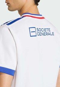 Bílý sportovní dres s modro-červeným proužkovaným límcem. Na horní části zad je modrý nápis „SOCIETE GENERALE“. Měkká textilie.